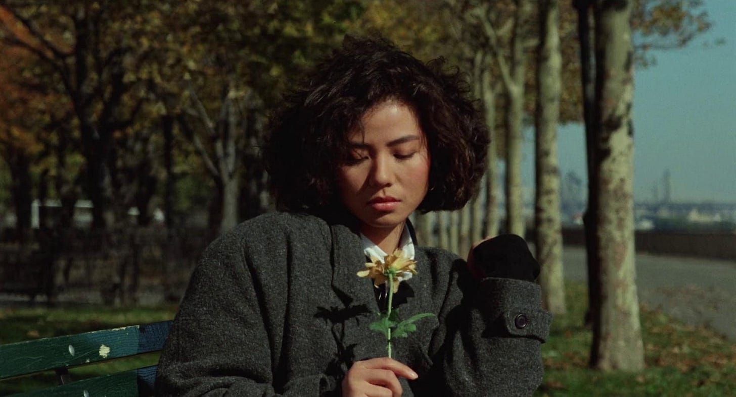 Sitting on a bench, Cherie Chung holds a flower against an autumnal backdrop in "An Autumn's Tale" (1987)