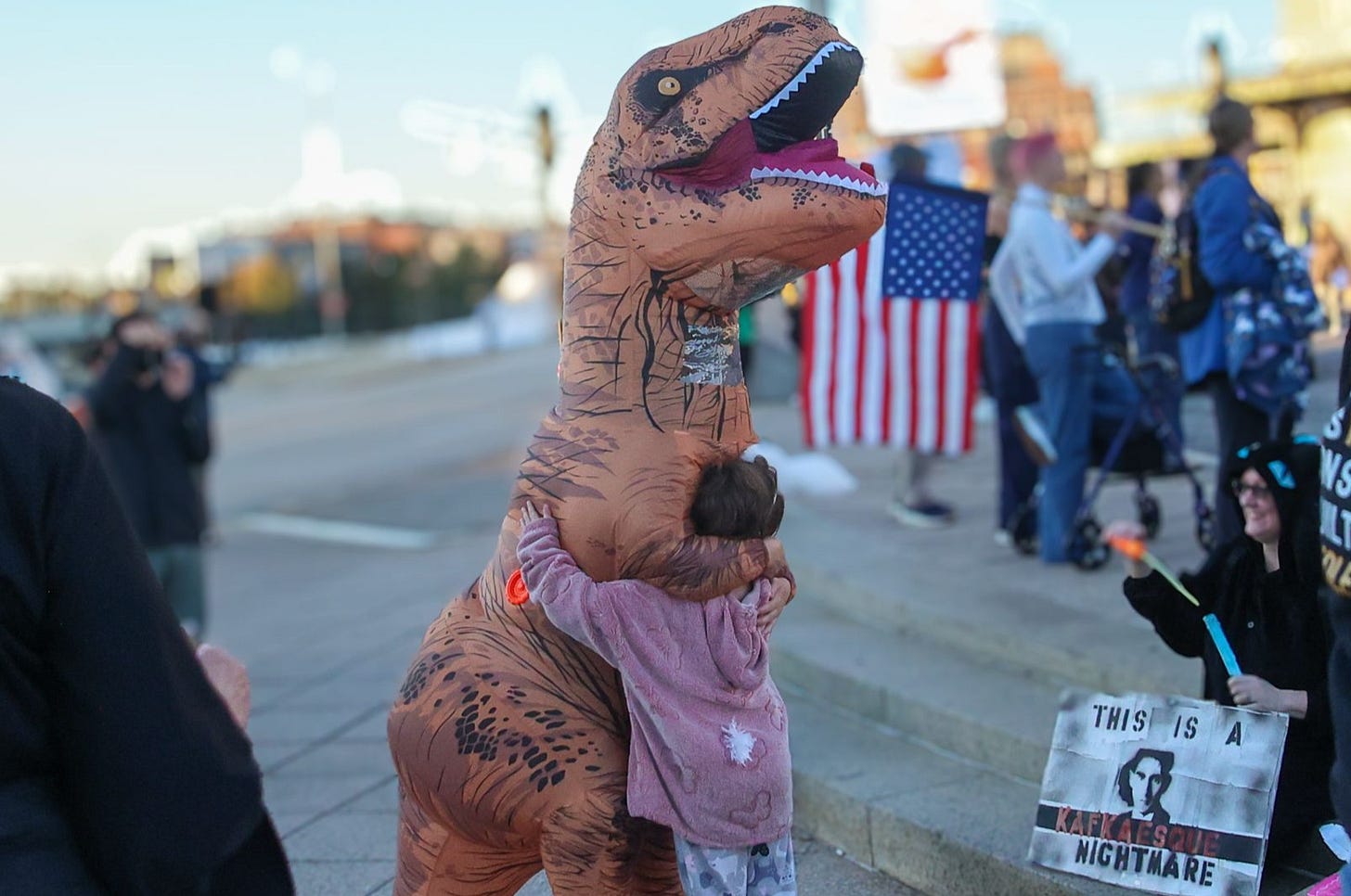 A child hugs a person in an inflatable dinosaur costume during a “No Kings” Dance Party at Baltimore’s Penn Station celebrating art, music, and community in a lively public event on October 18, 2025. (Photo by Robyn Stevens Brody/Sipa USA via AP Images)