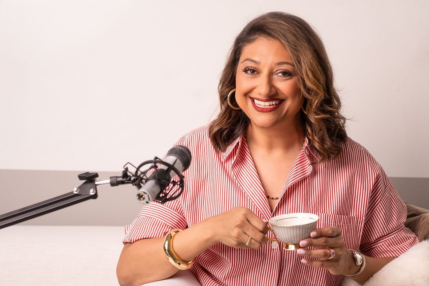 Deepali Vyas at a microphone holding a cup of tea