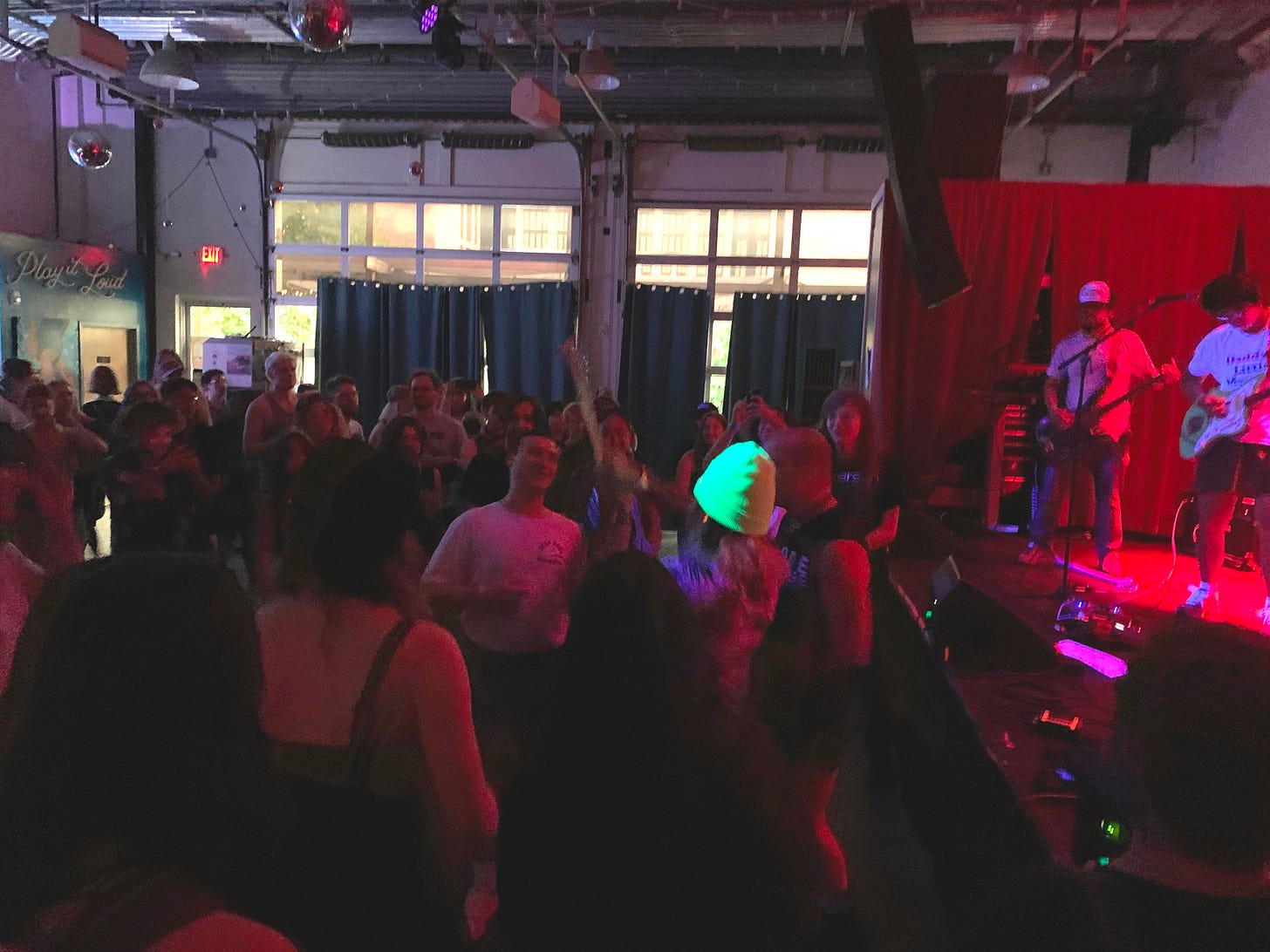 Aaron from Cuni playing guitar in an energetic crowd while Jared, in a "Daddy's Little Meatball" shirt, plays onstage.