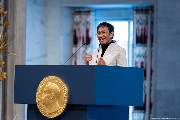 Maria Ressa speaking on 10 December 2021. She is delivering her Nobel Prize lecture wearing a white blazer and glasses.