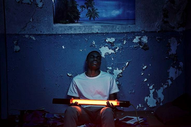 This may contain: a man sitting on the floor holding a glowing object in front of his face and looking up