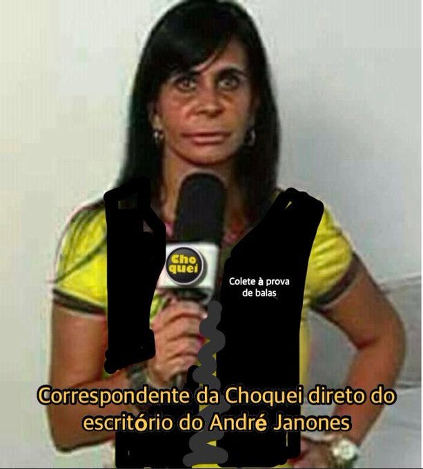 gretchen segurando microfone do choquei com cara séria. pintaram mal pintado um colete nela onde tá escrito "colete à prova de balas". na legenda: correspondente da choquei direto do escritório do andré janones