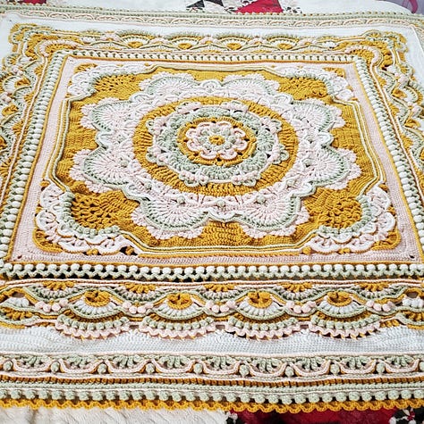 A crocheted mandala afghan blanket in goldenrod, sage, pink, and white.