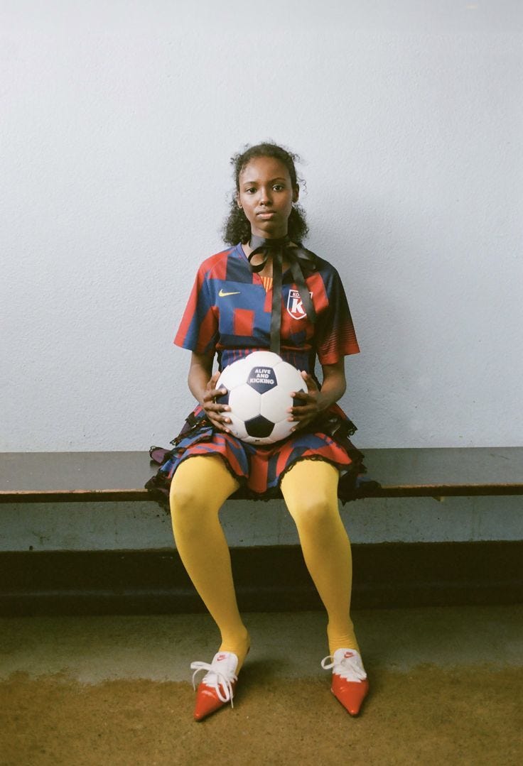 This may contain: a woman sitting on a bench with a soccer ball in her hand and wearing yellow socks