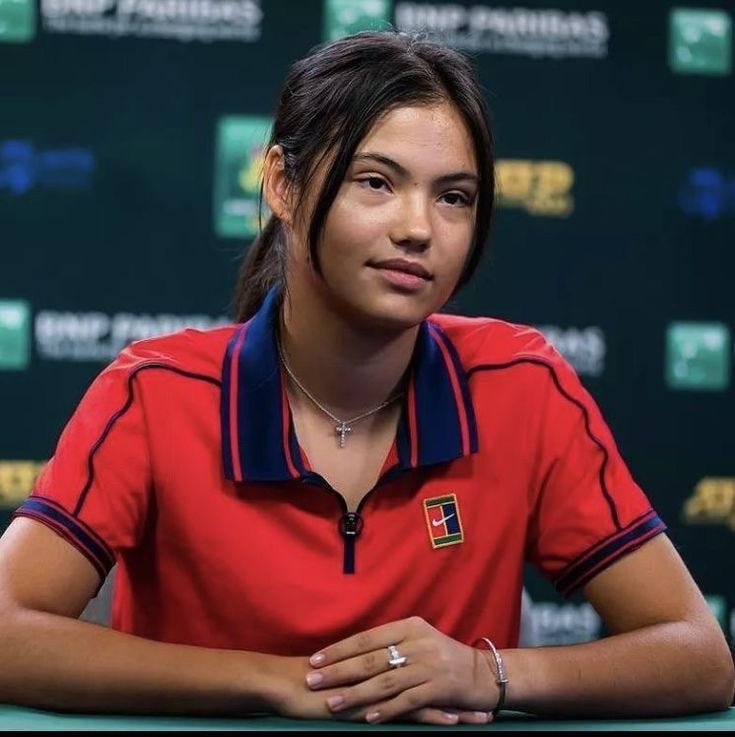 This may contain: a woman sitting at a table with her hands folded in front of her chest and wearing a red shirt