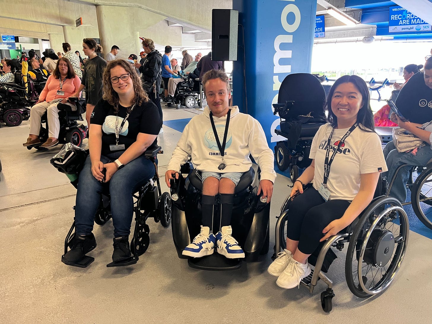 Amy, Jaden, Olivia smiling at the camera in their wheelchairs in front of many other wheelchair-using participants at Eden Park Amy, Jaden, Olivia smiling at the camera in their wheelchairs in front of many other wheelchair-using participants at Eden Park