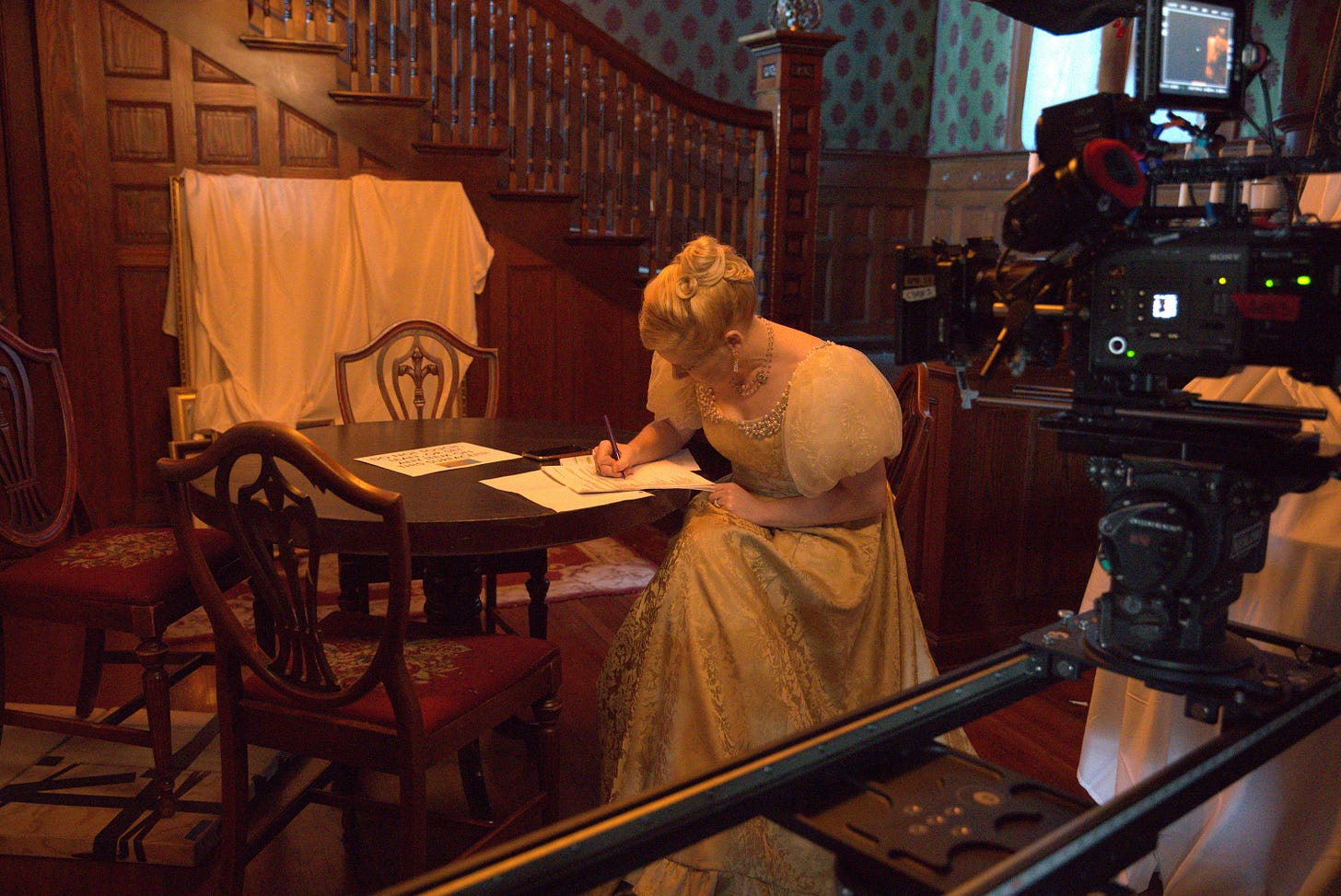 An actress sits at a table writing while a camera films her An actress sits at a table writing while a camera films her