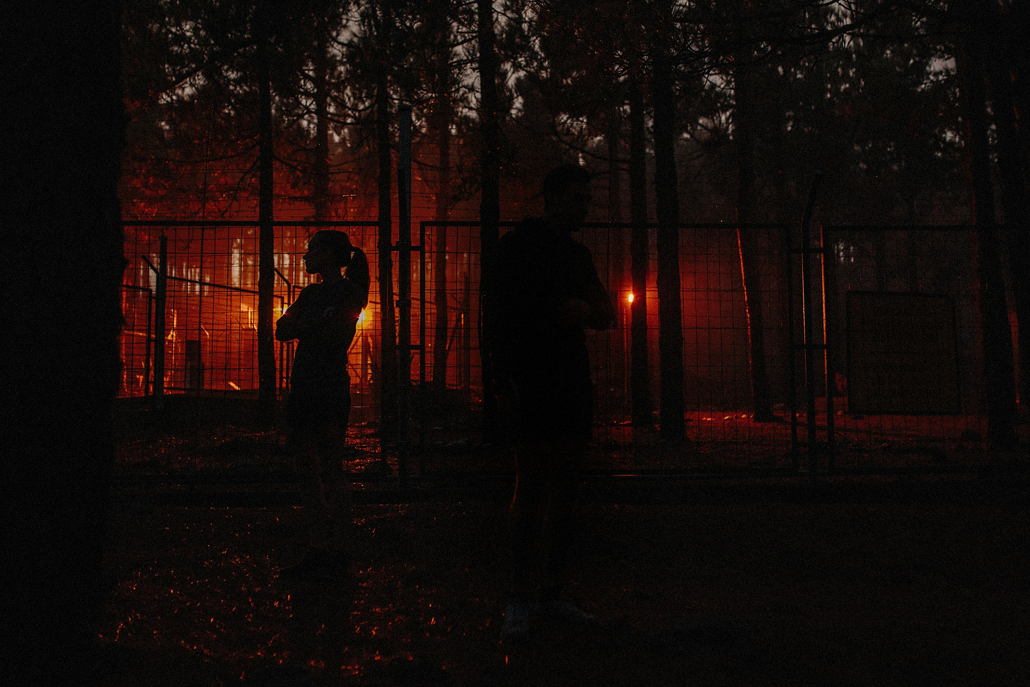 Two runners standing in front of a fence all red and black evening sun covered