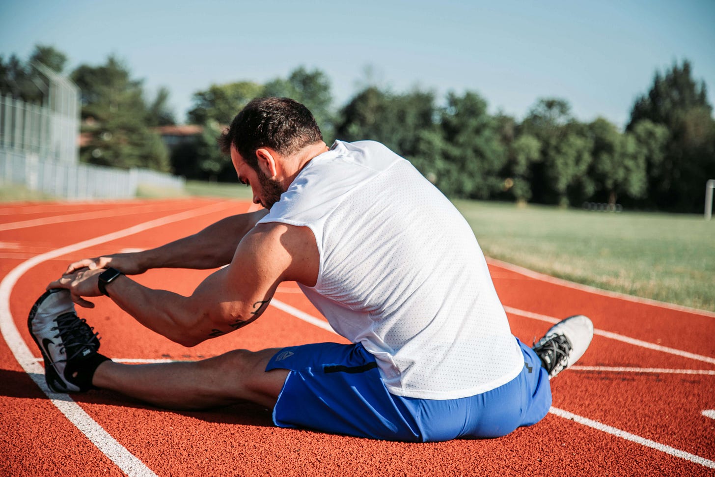 Male athlete stretching outdoors in a forest, representing post-workout recovery and relaxation.
