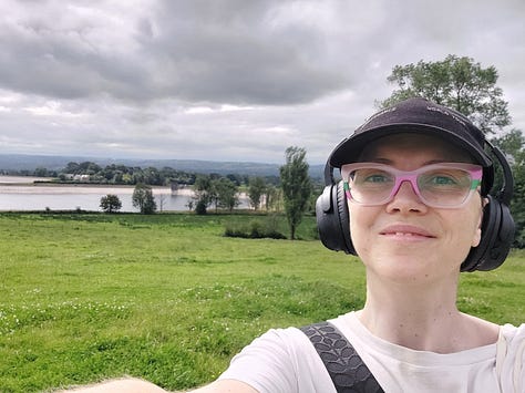 Smiling selfies of me mid walk. Behind me you see pink blooming Himalayan Balsam. In another picture is a straight grey road disappearing into the horizon. In another is a body of water, some grey clouds and lush grass in the foreground. Other pictures are of nature, a close up of an orange and black painted lady butterfly, dappled sun shining through woodland pines and a canal with reeds along its edge and algae on the water