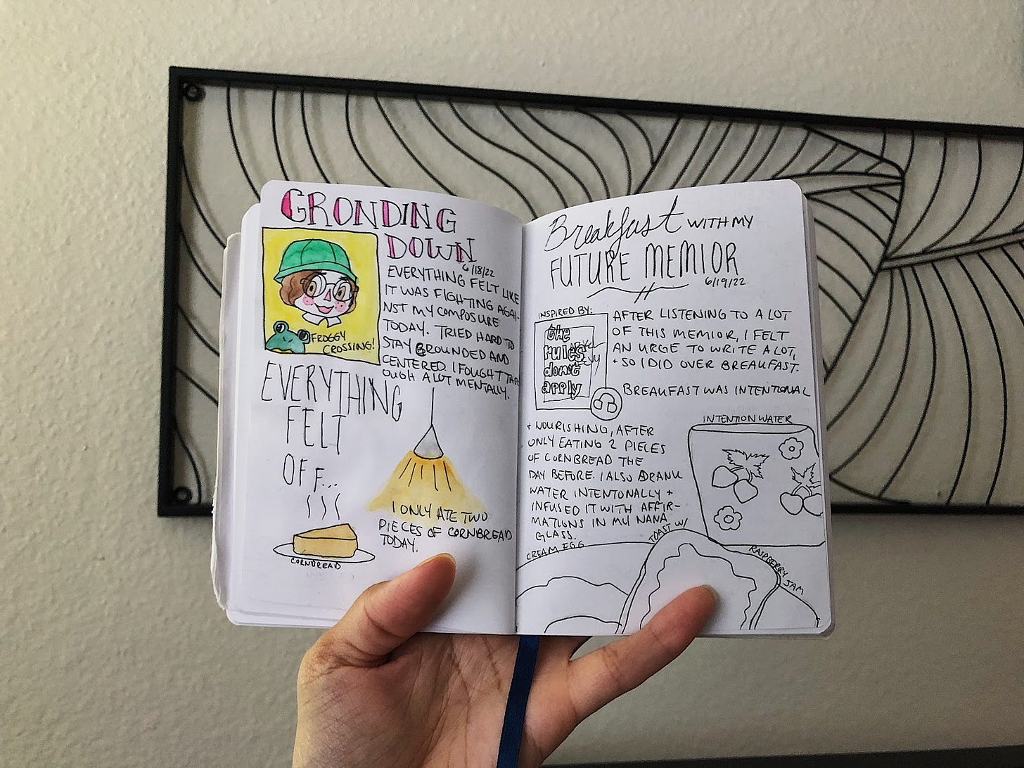 Watercolor and ink on a small art journal being held open in the air with a wall background