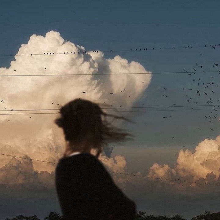 This may contain: a woman standing in front of a large cloud with birds flying over her and power lines