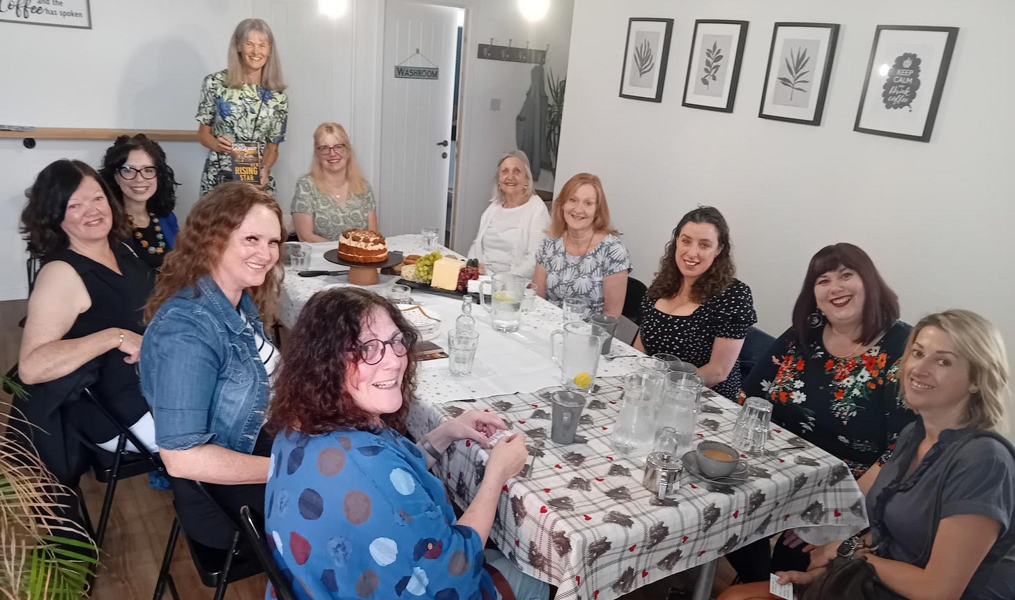 Guests at a table of drinks and food. Crime fiction author Rachel Sargeant stands in the background.