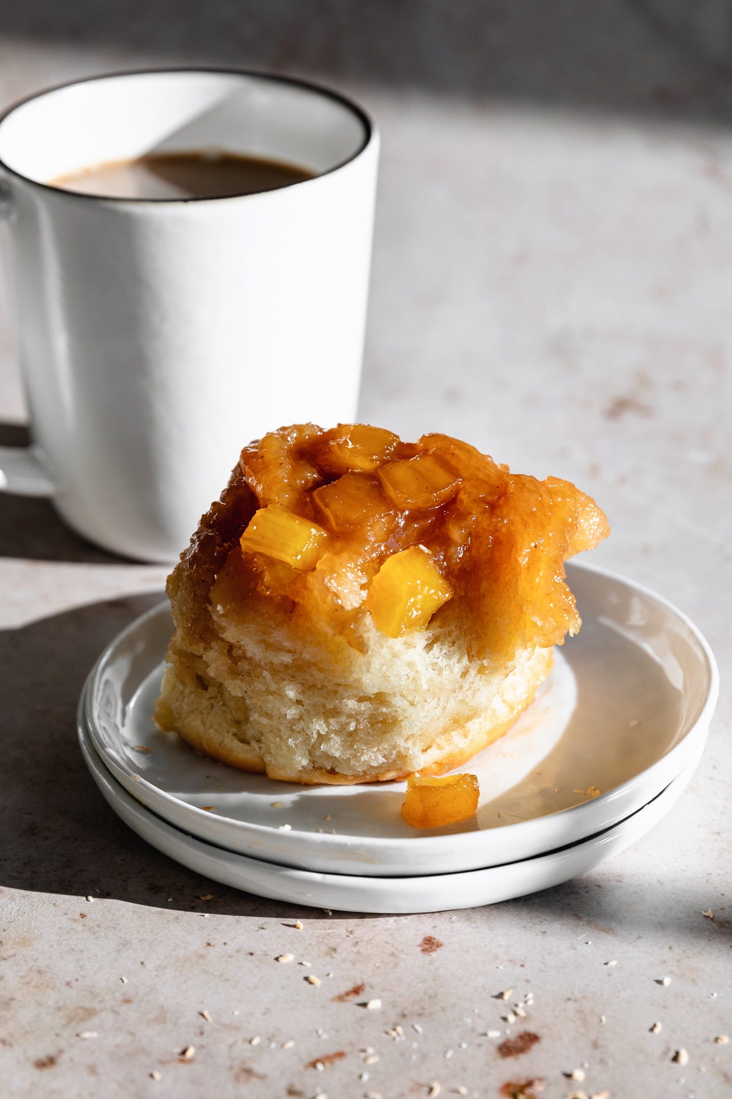 Vegan pineapple coconut sticky bun on white plate with white coffee cup
