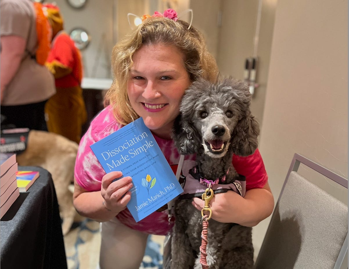 Jamie poses with a copy of Dissociation Made Simple while hugging a grey poodle named Starlight. Both are smiling! Jamie poses with a copy of Dissociation Made Simple while hugging a grey poodle named Starlight. Both are smiling!