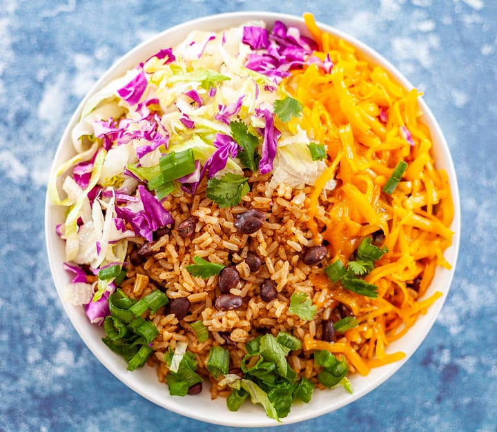 Rice and bean burrito and a burrito bowl with grated cheese and toppings.