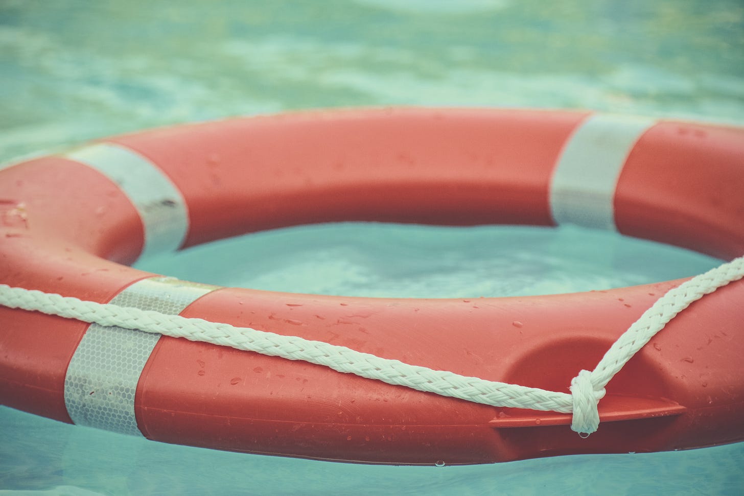 A red and white life raft floats on blue-green water. A red and white life raft floats on blue-green water.