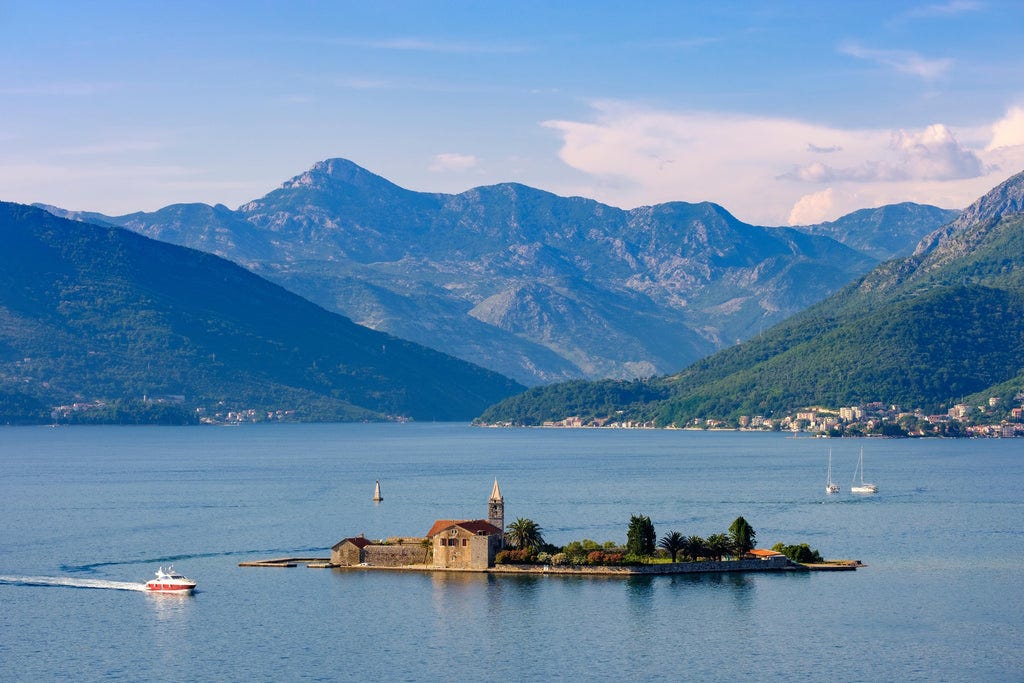 a small island in the water with a building and boats in the background