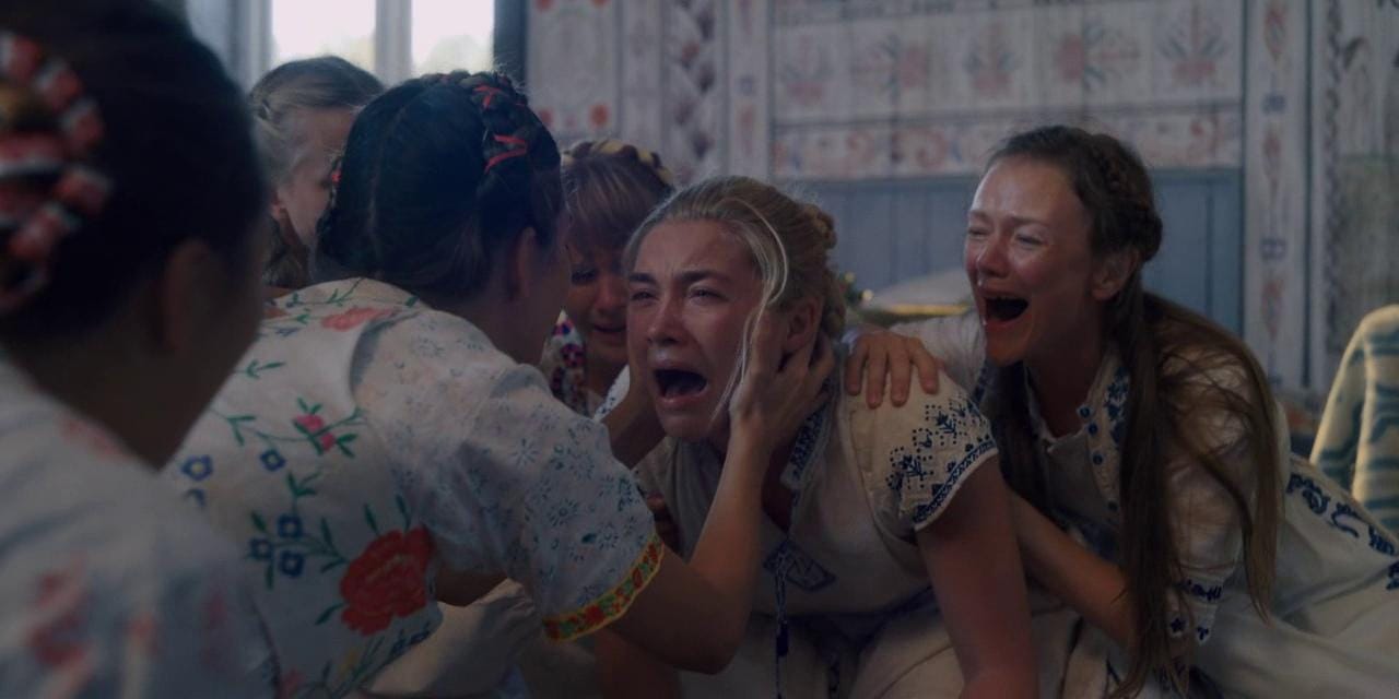 Dani wails, while another woman holds her face. She is surrounded by wailing women, all on the floor on all fours.