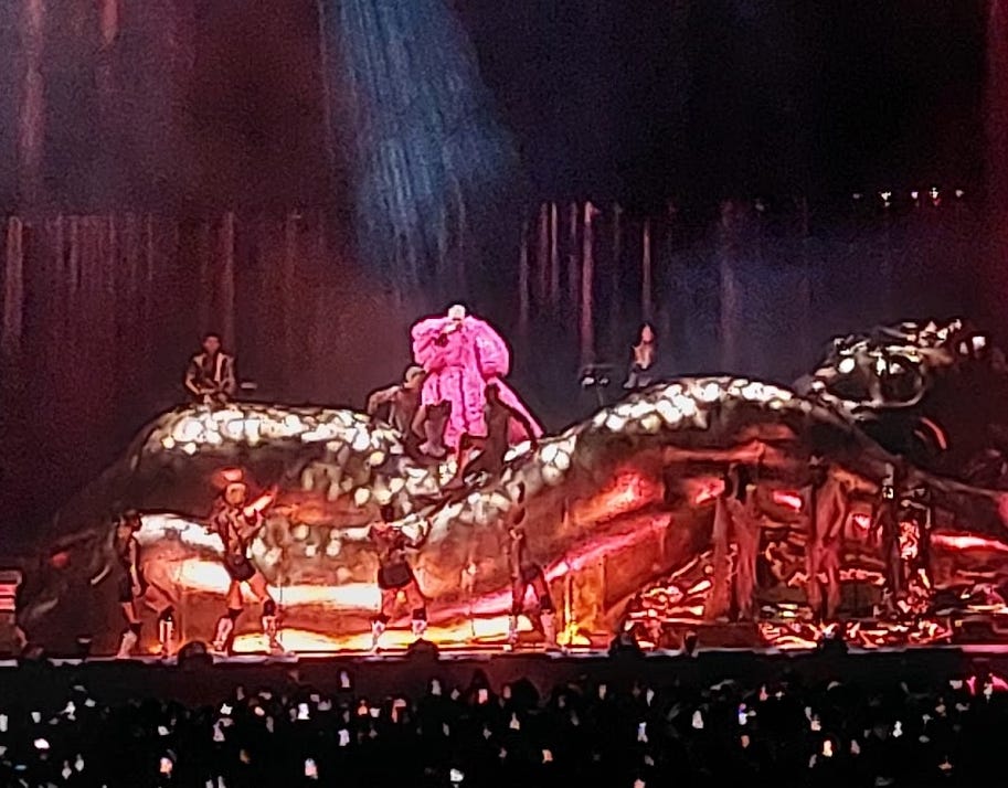 Sam Smith wearing their iconic billowing pink dress from the I'm Not Here to Make Friends video surrounded by their dancers and band