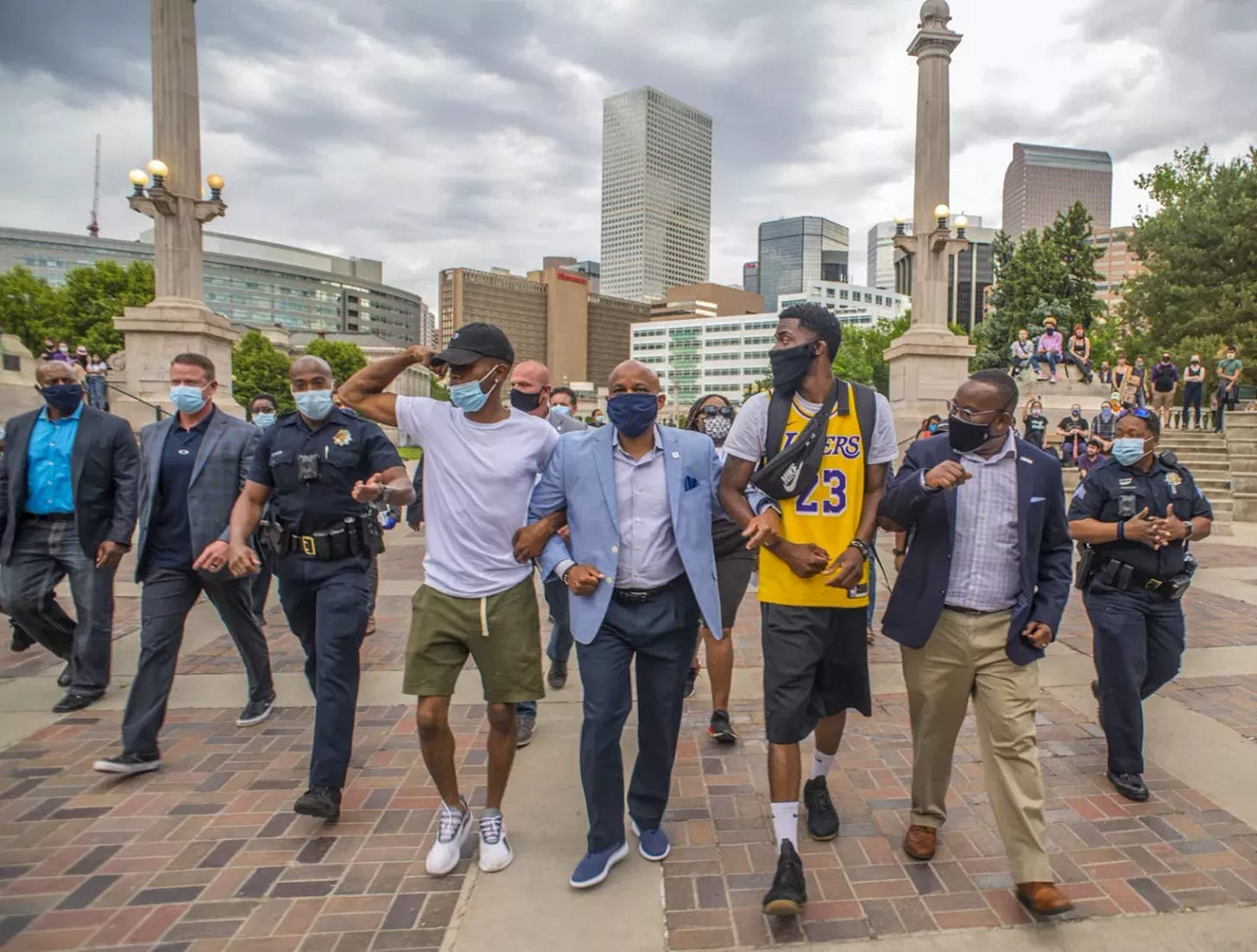 Michael Hancock walking in the middle of a group with arms linked with two others and police flanking either side
