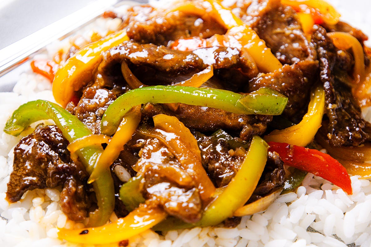 A beef and pepper stir fry with onions on a bed of white rice.