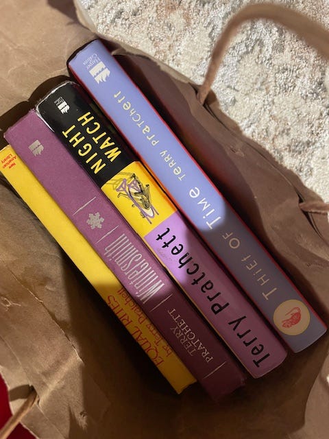 Several Terry Pratchett books in a paper bag: Equal Rights, Wintersmith, Night Watch, and Thief of Time.