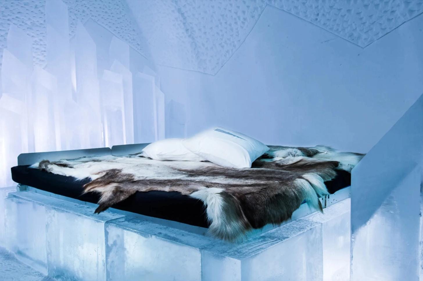 Ice hotel bedroom featuring an ice bed frame covered with thermal bedding and reindeer hides.