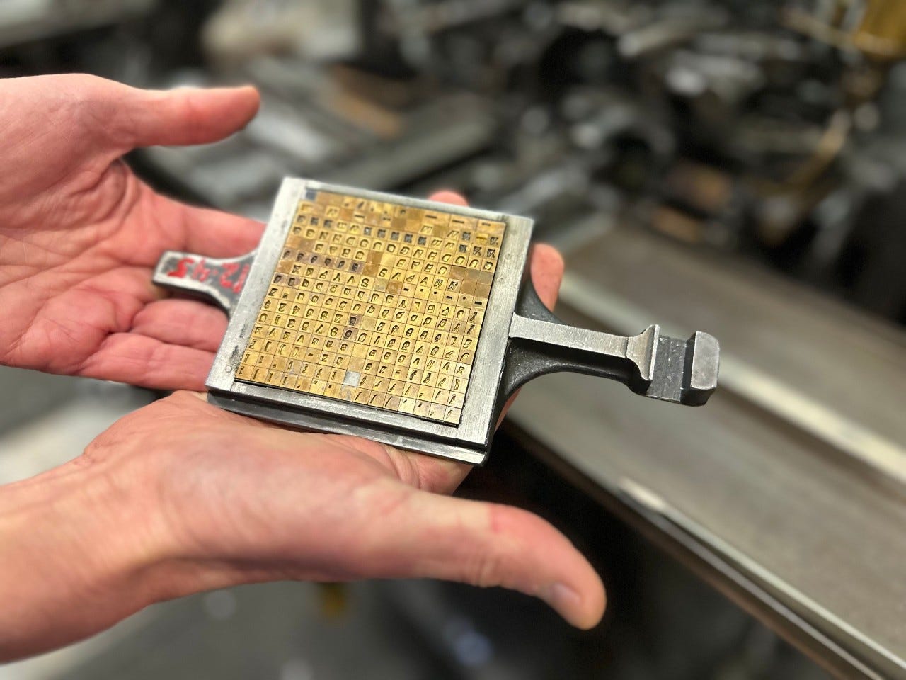 Close-up of hands holding a vintage metal printing plate filled with brass type blocks used in letterpress printing