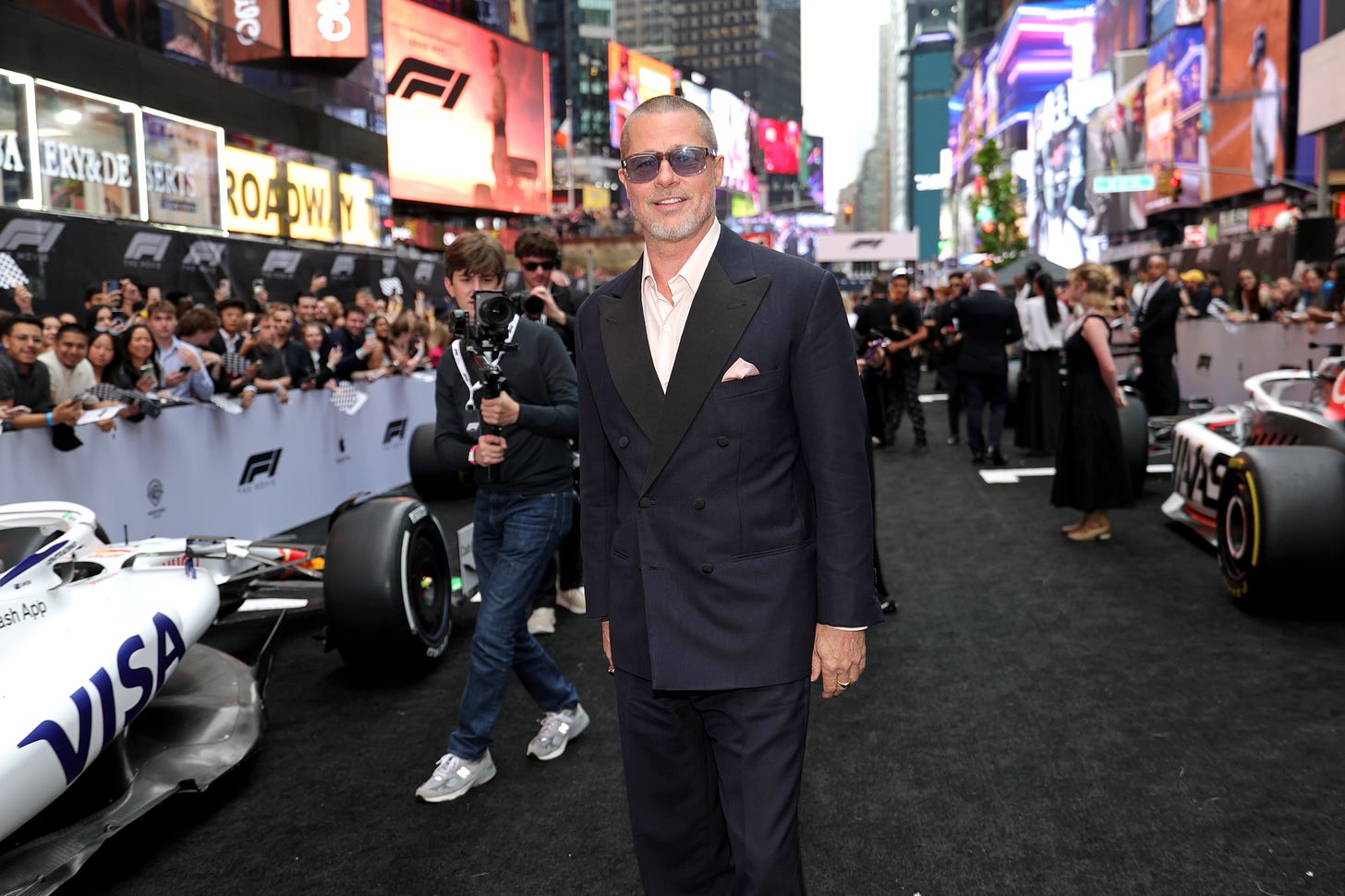 Brad Pitt wearing a dark blue suit and sunglasses as he walks past F1 cars in Times Square at the world premiere of F1: The Movie Brad Pitt wearing a dark blue suit and sunglasses as he walks past F1 cars in Times Square at the world premiere of F1: The Movie