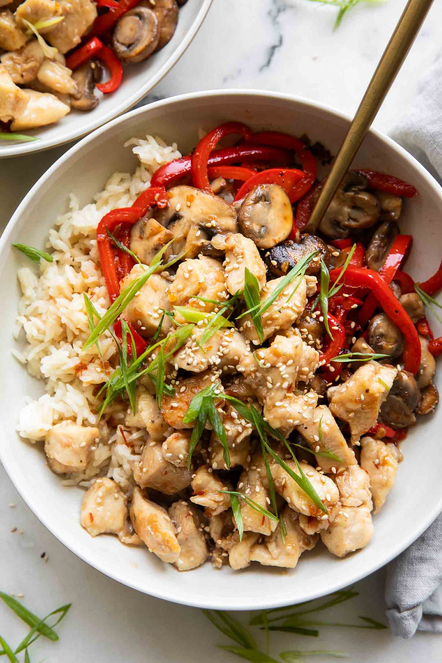 A general tso's chicken bowl with rice, topped with scallions and white sesame seeds. 
