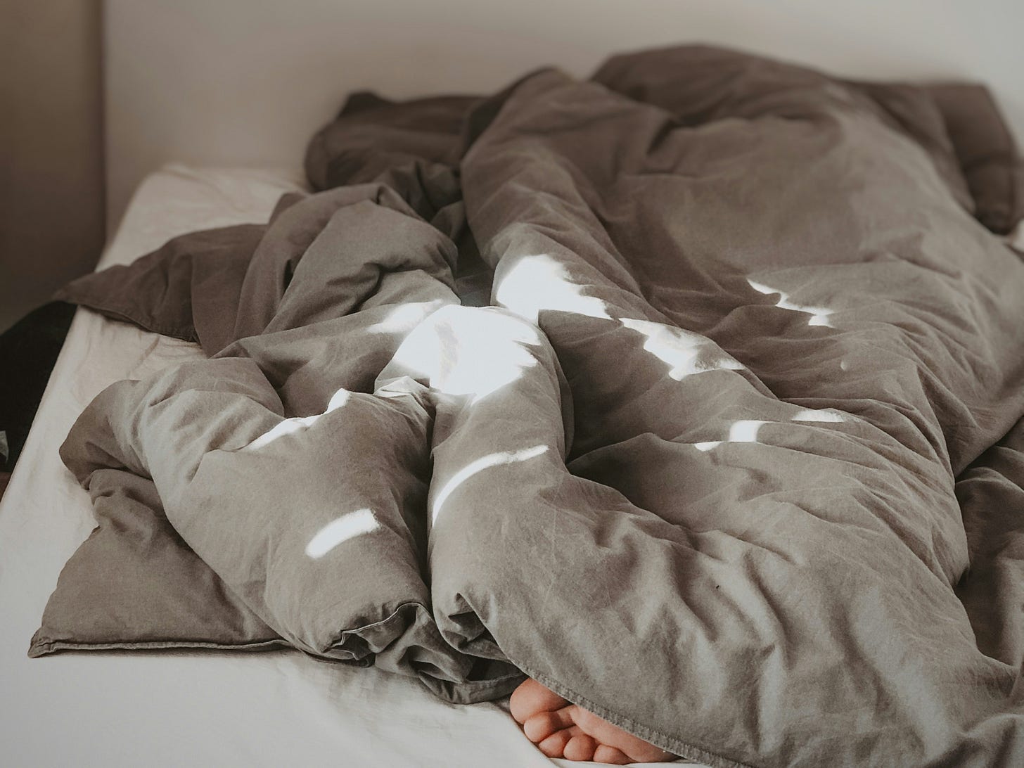 A bare foot peeks out from under a messy grey and white bedding.