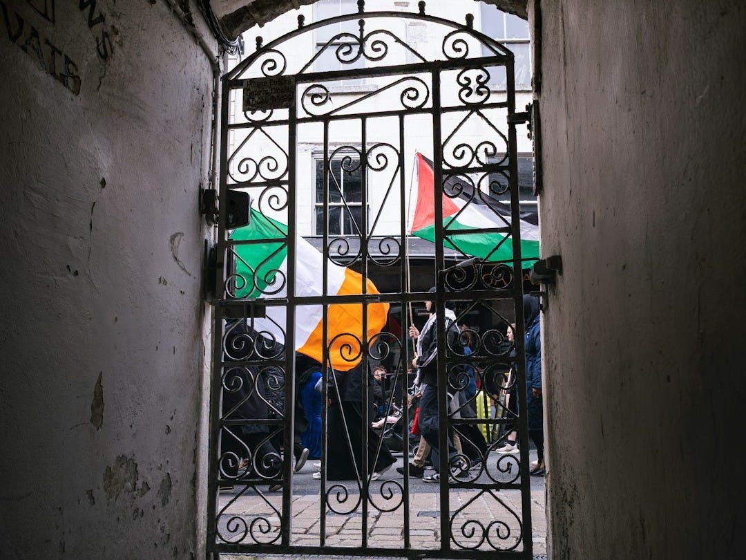 View through a gate and archway with irish flags.