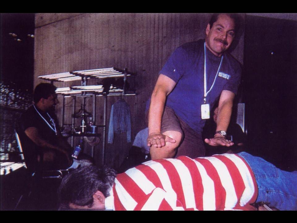 Chiropractor in a blue shirt and lanyard adjusts the back of a man lying face down in a red and white striped shirt