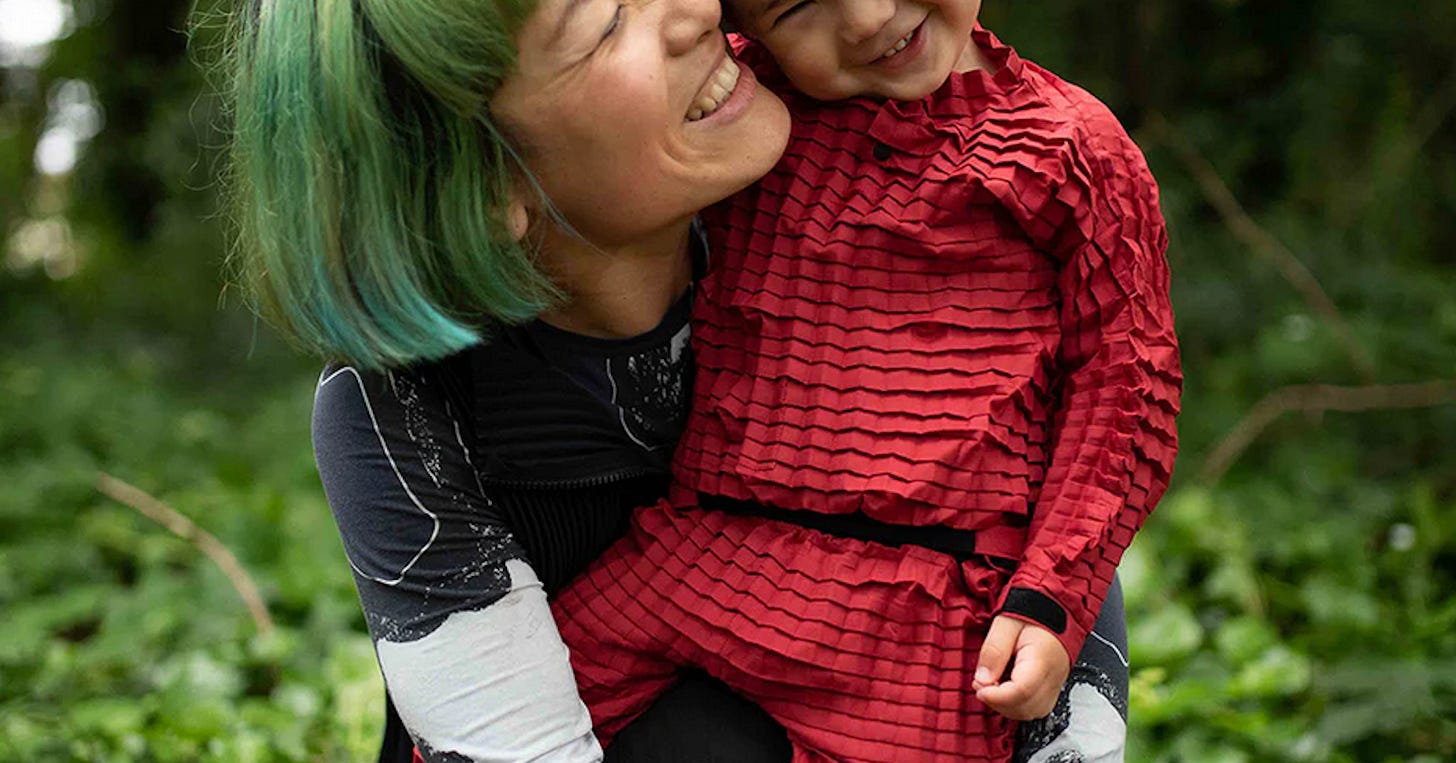 A child in a Petit Pli outfit being hugged by his mum