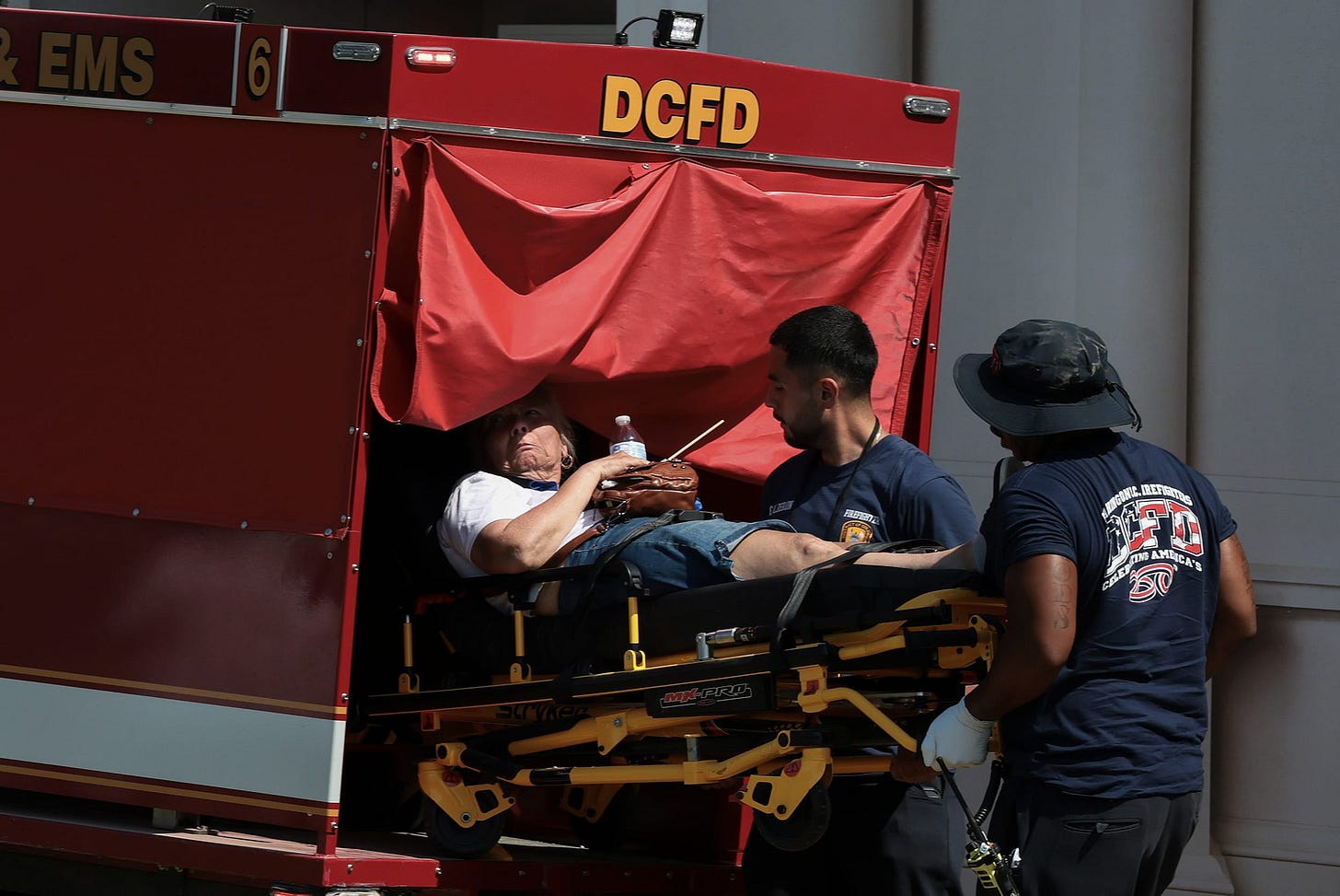 Two paramedics lifting a person on a stretcher into a red emergency vehicle.