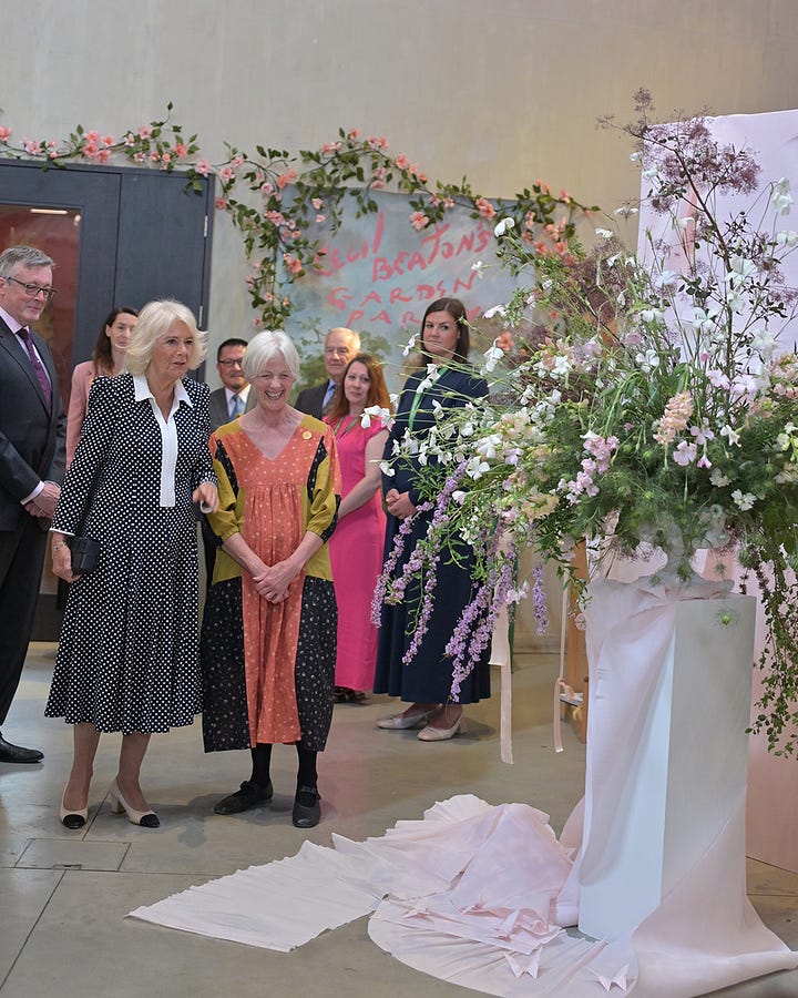 2 people including the queen by flowers