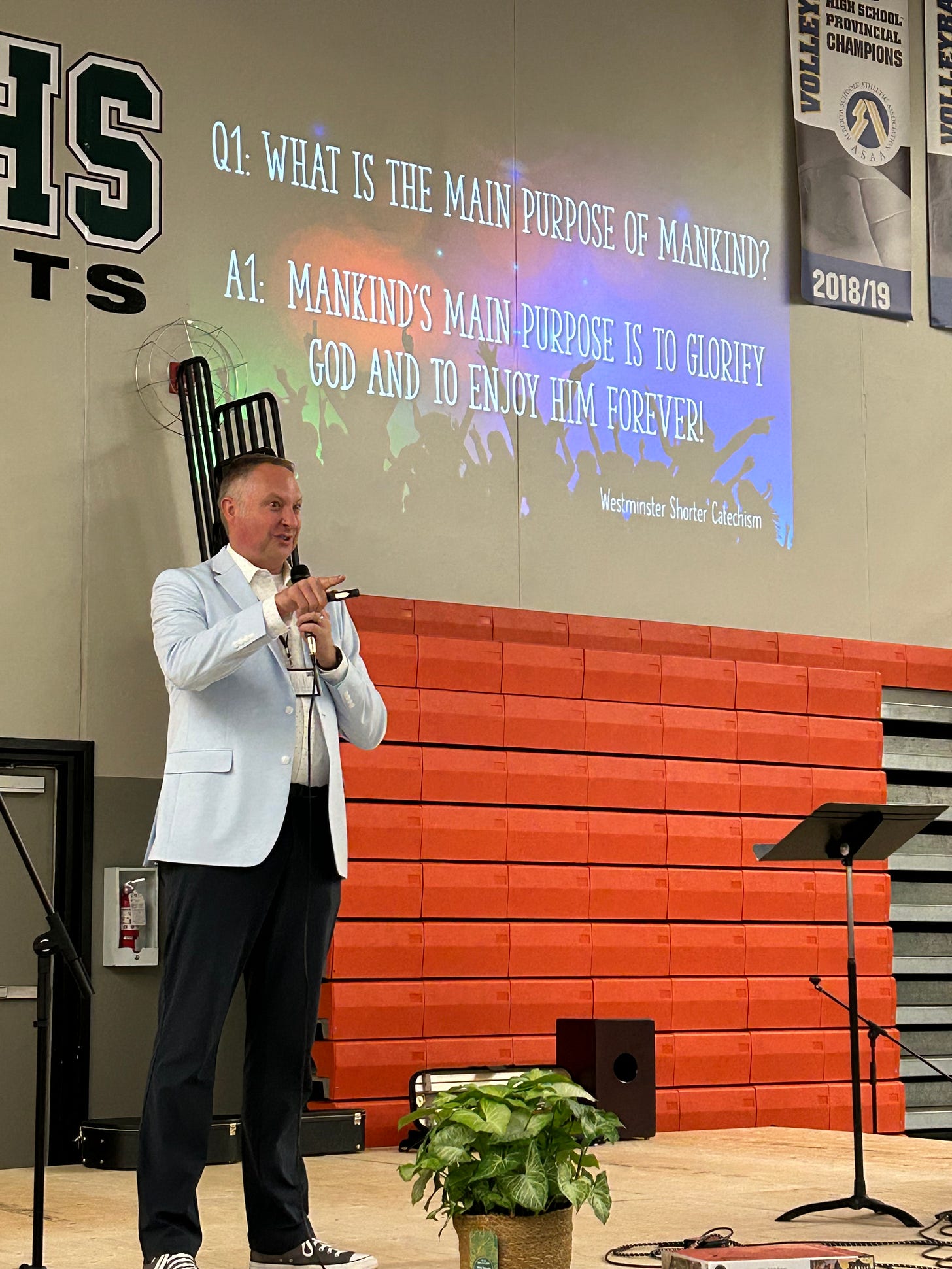 Dr. Dave on stage with the text of Westminster Shorter Catechism Q&A 1 projected behind him.