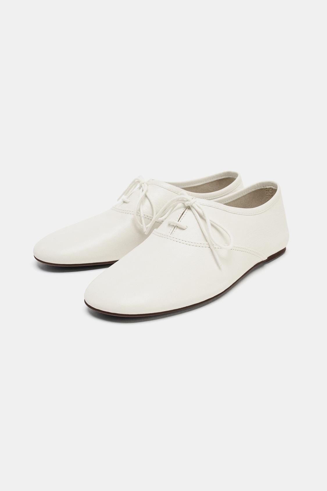 White lace-up shoes with a round toe and a flat brown sole. White lace-up shoes with a round toe and a flat brown sole.
