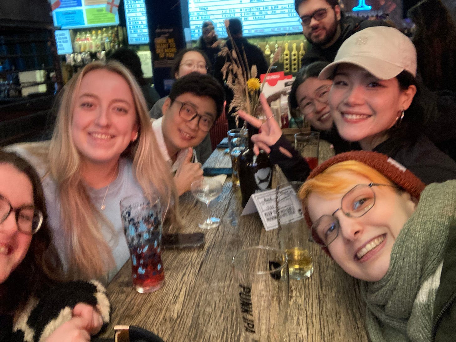 Selfie of eight researchers on a long wooden table in a bar, with pint glasses of varying fullness lined up down the table. 