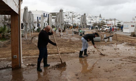 People sweep mud away outside a building next to tied-up parasols on a cloudy day
