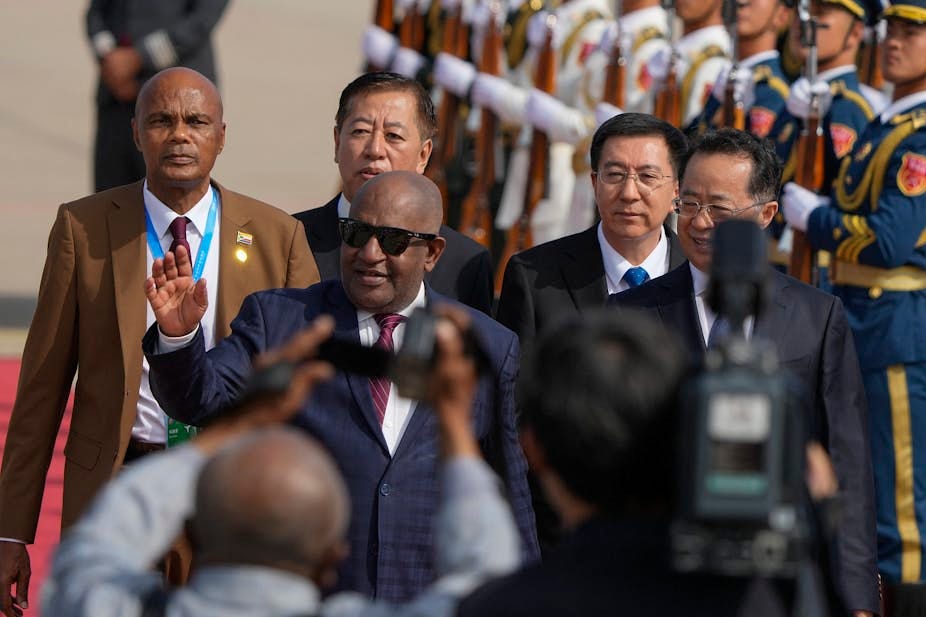 A man wearing sunglasses waves as he walks past a military guard. A man wearing sunglasses waves as he walks past a military guard.