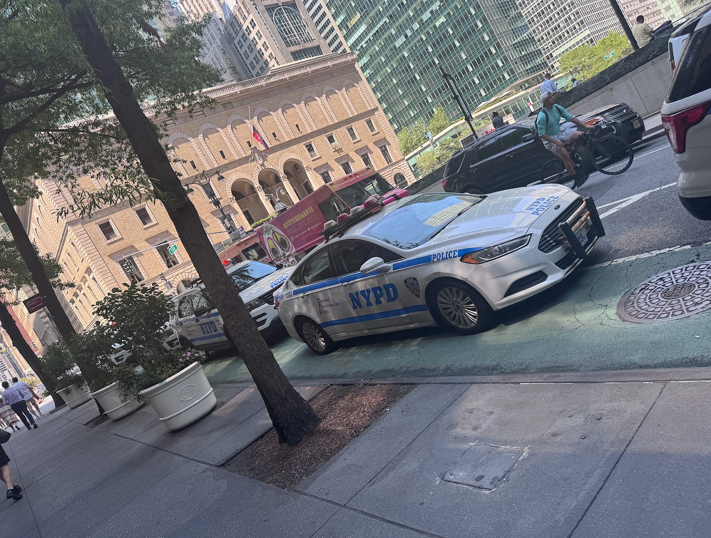 Five New York Police Department vehicles are parked in a row on a busy NYC street.