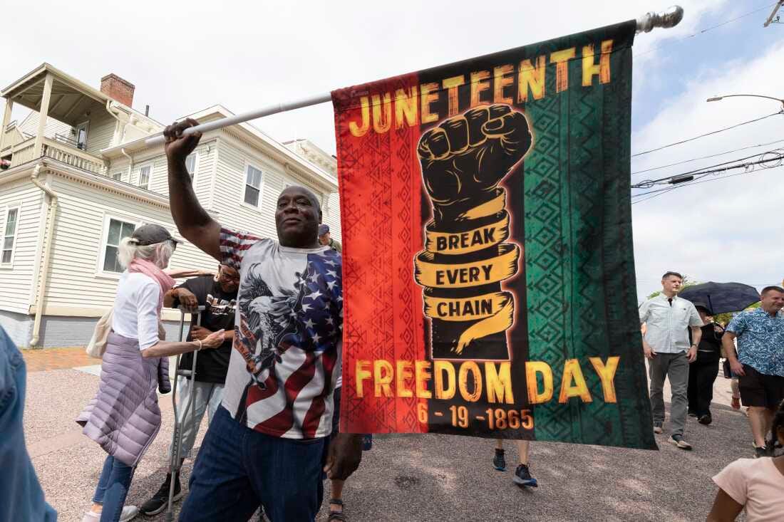 Robert Reid holds a flag with the words "Juneteenth Freedom Day" and "break every chain" on it. 