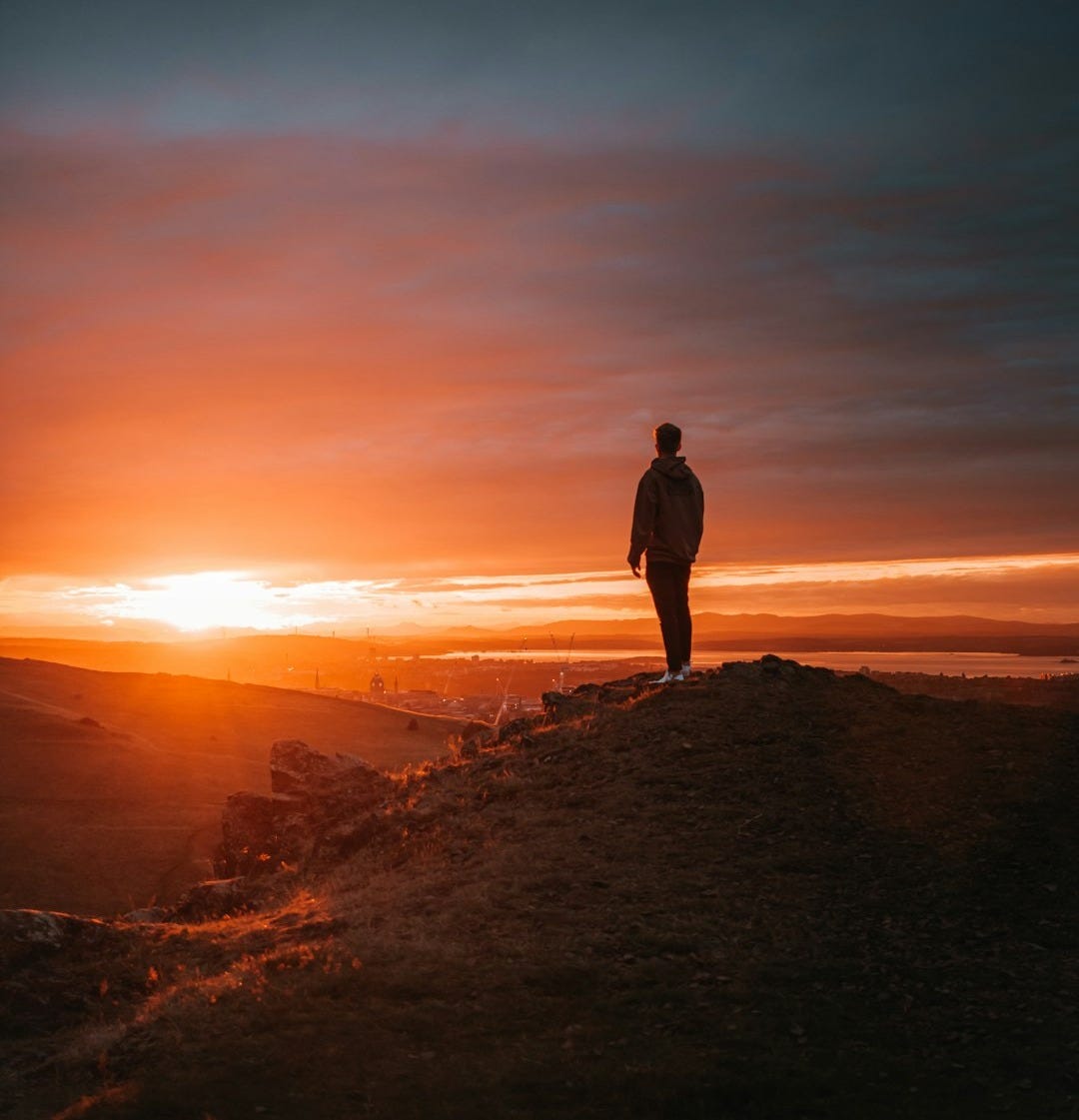 man in black jacket standing on brown rock during sunset man in black jacket standing on brown rock during sunset