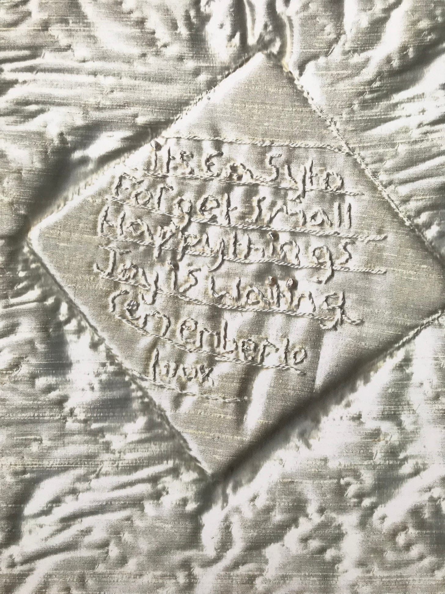 Book of Hours cover, image of quilted satin fabric with stitching in a diamond shape at the centre with the text "It’s easy to forget small happy things joy is waiting remember to look."  in hand stitch.
