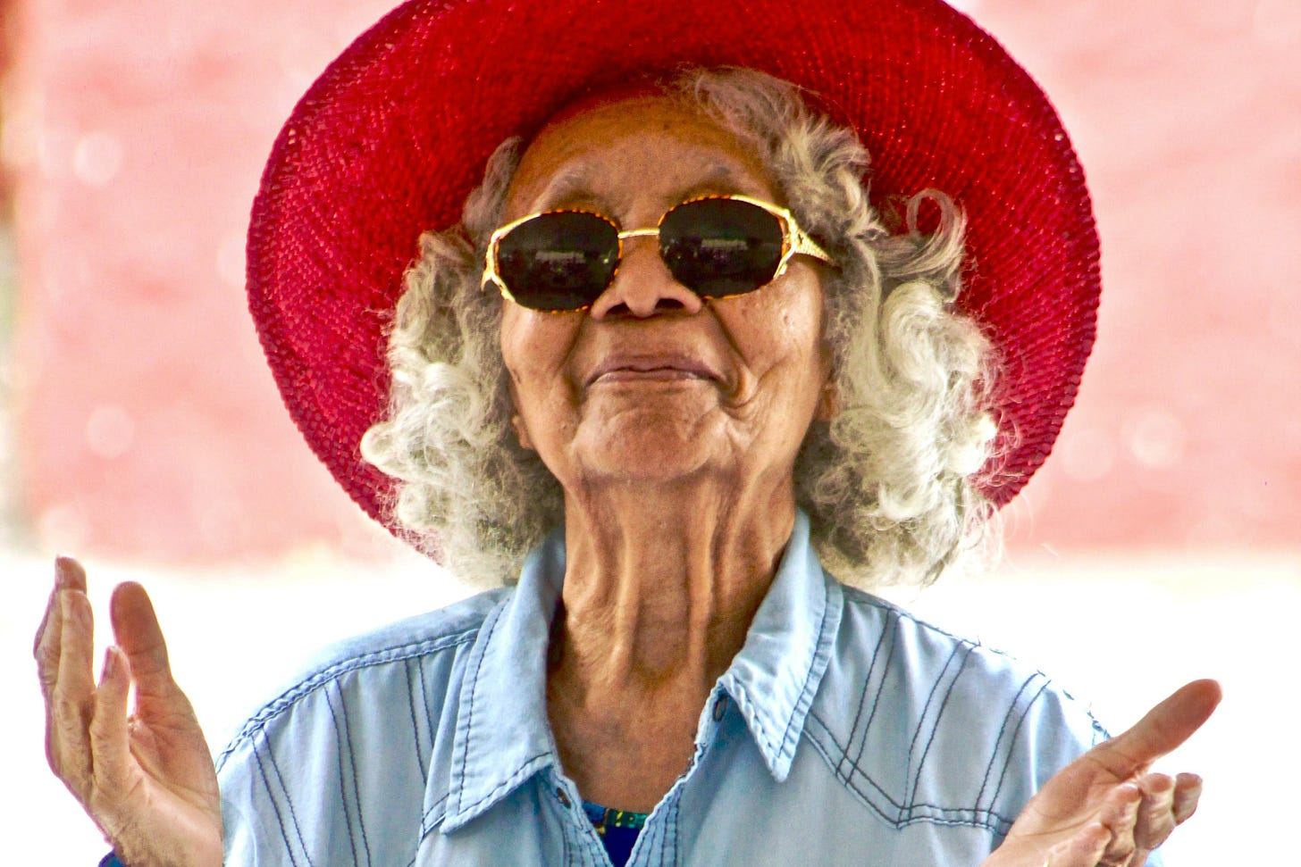 Older woman in red straw hat and sunglasses lifts her hands skyward in prayer Older woman in red straw hat and sunglasses lifts her hands skyward in prayer