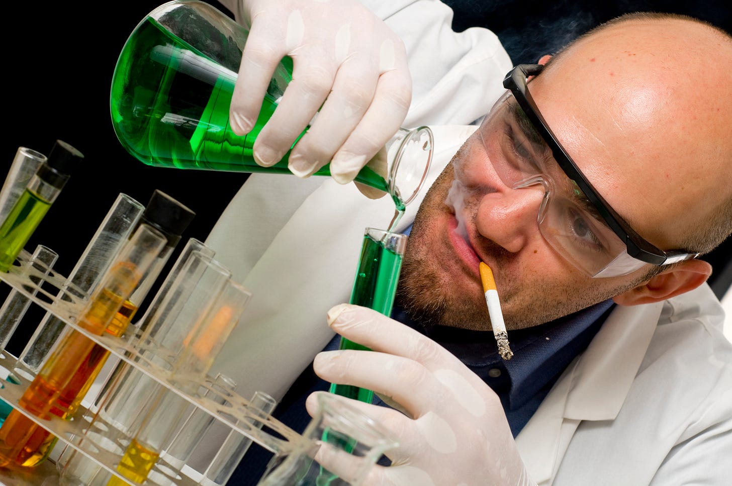 A scientist working with lab chemicals whilst smoking a cigarette. He has a devilish grin on his face.