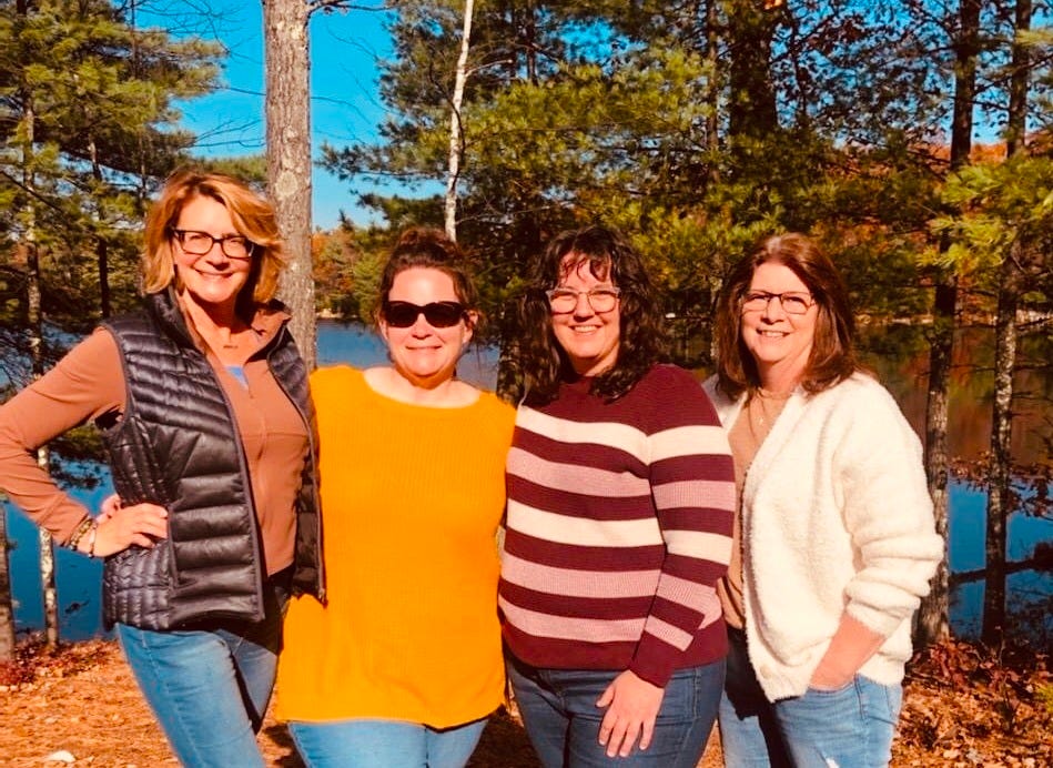 Picture of four woman standing in front of a lake in the fall. 